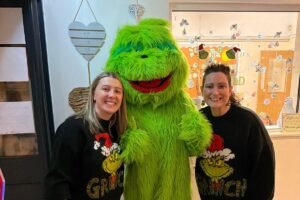 Two Rowans Day Nursery team members in Grinch Christmas jumpers standing with the Grinch