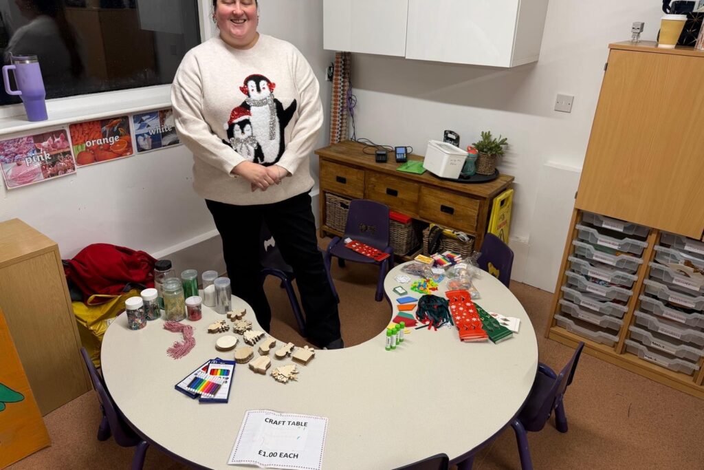 A Christmas craft table with wooden decorations, glitter and pens at a Rowans Day Nursery Christmas fete